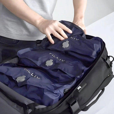 A person settling three Midnight Blue TILLIV Stak packs side by side into a black travel backpack